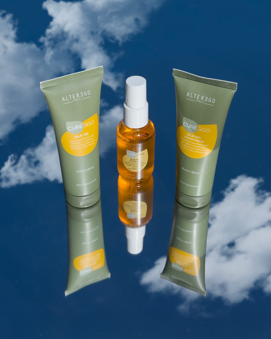 CurEgo Silk Oil complete trio — Shampoo Conditioner and Blend Oil on reflective blue sky surface by Alter Ego Italy